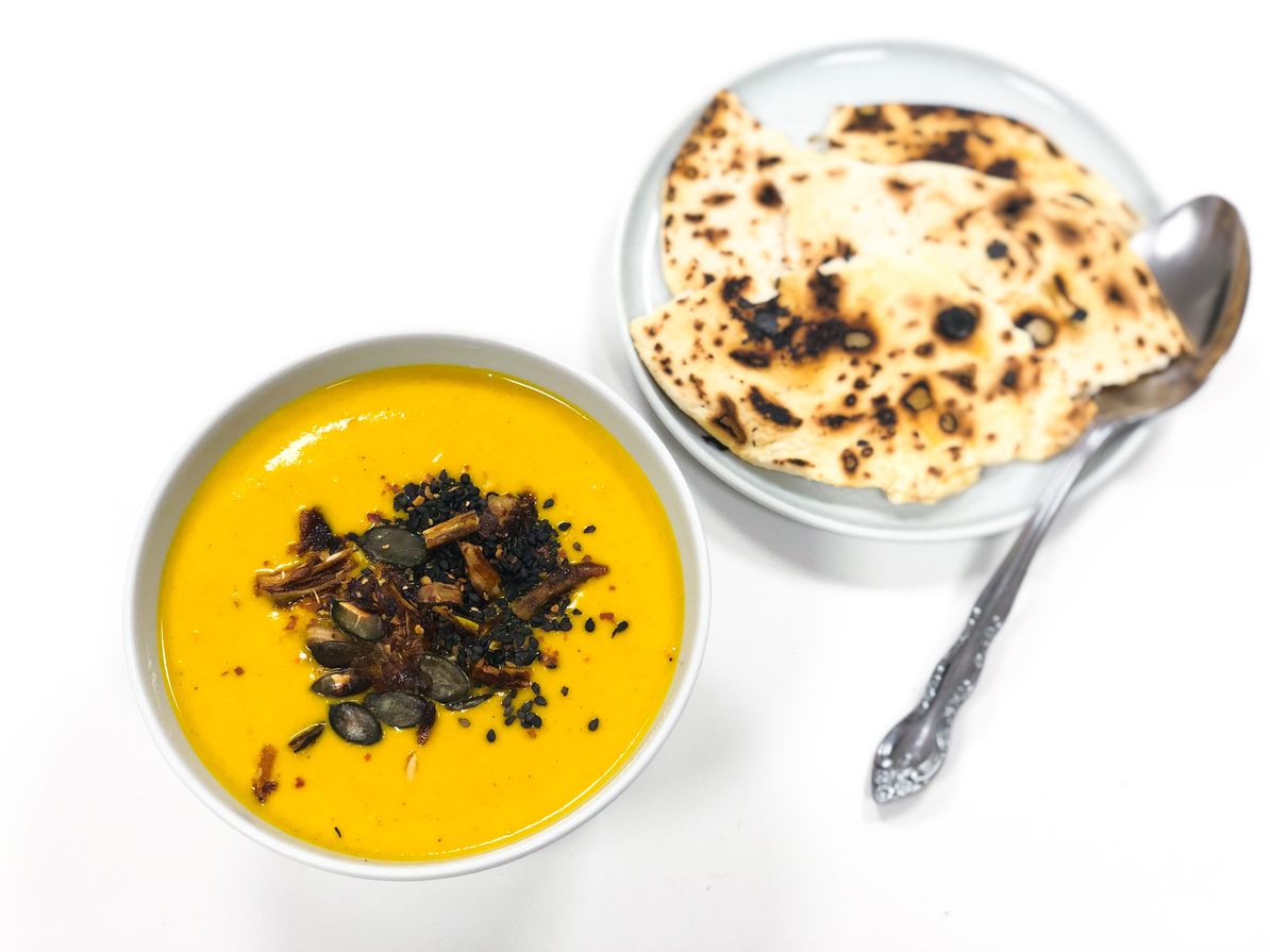 slika recepta: korenčkova juha, servirana v keramični posodici, posuta z mešanico semen, zraven je postrežen chapati kruh