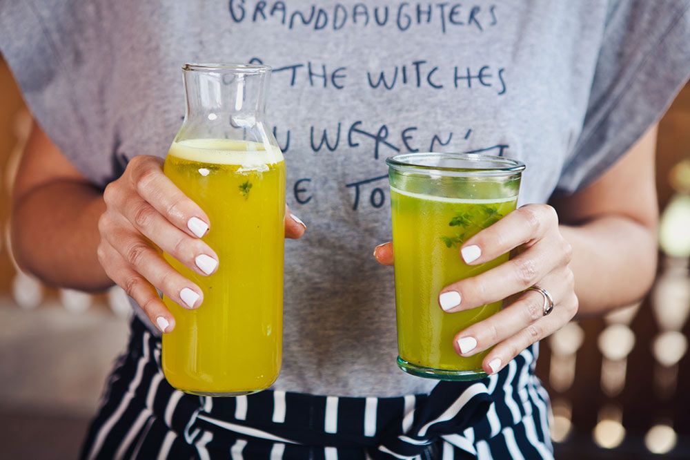 Oseba drži v roki steklenico in kozarec fermentiranega citrusnega napitka