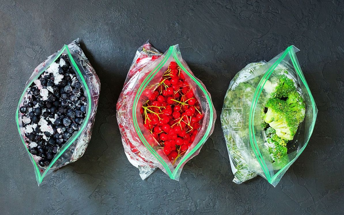 3 vrečke napolnjene z zamrznjenim sadjem in zelenjavo na temni podlagi