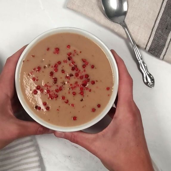 slika recepta - pumpkin spice kostanjeva juha, servirana v svetli skodelici, posuta z rdečim poprom, zraven je žlica