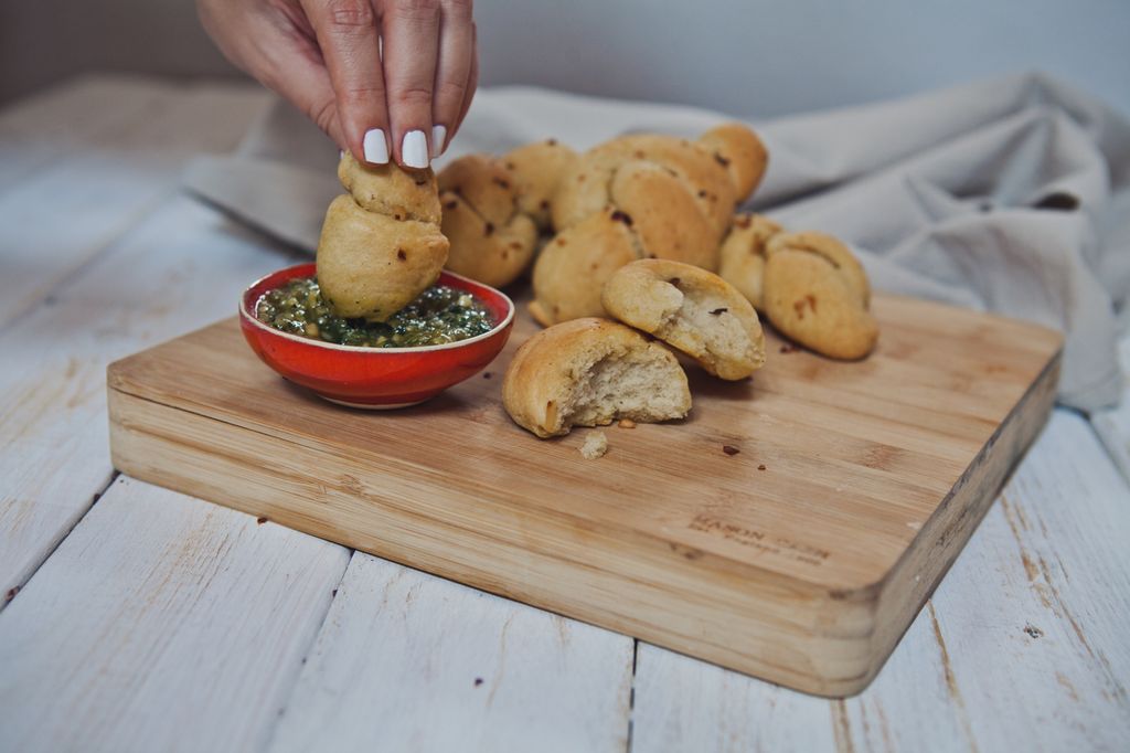 ženska roka pomaka kruhov vozel v česnovo omako, na mizi je še več kruhovih vozlov