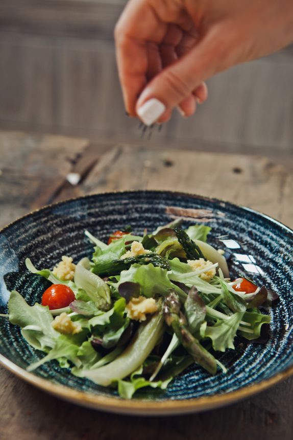 slika recepa: pomladna solata s cikorijo, servirana v keramični skodelici na mizi, roka po njej posuva rikoto