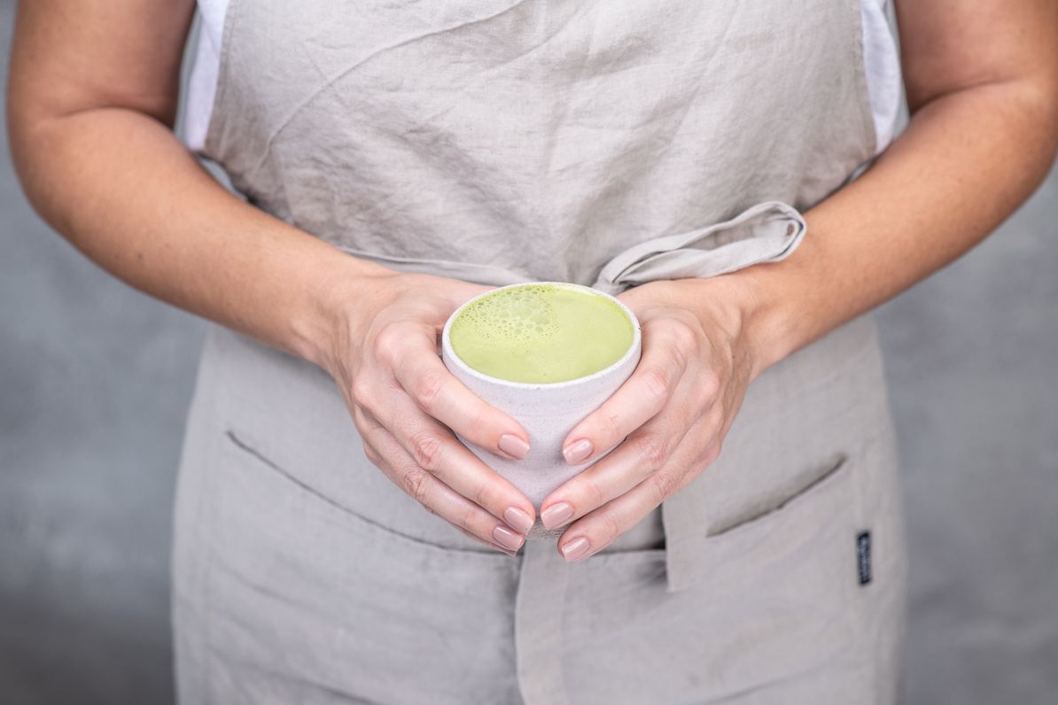 ženska v rokah drži keramično skodelico z zelenim matcha latte napitkom