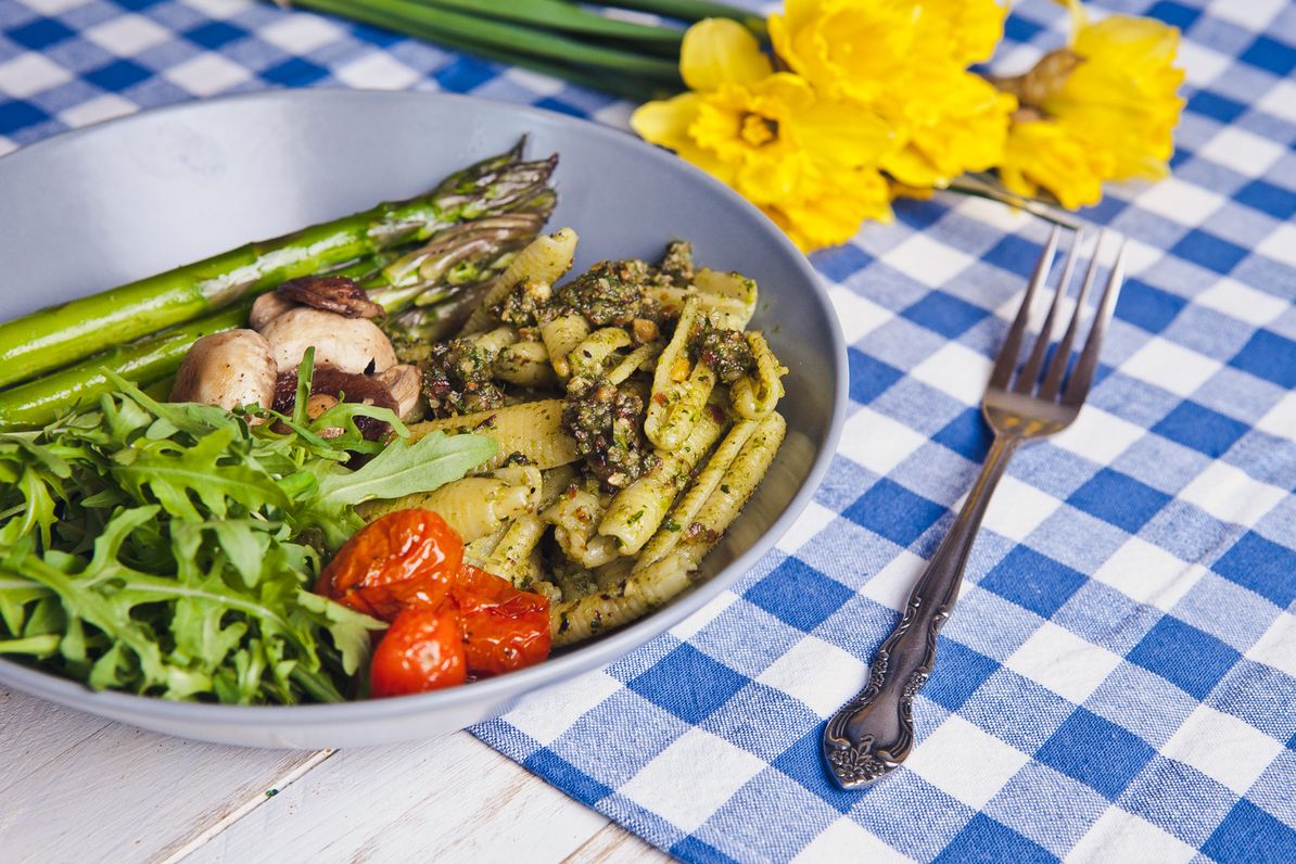 Spomladanska zelena testeninska skleda s šparglji, servirana v krožniku na mizi, zraven vilice in šopek narcis.