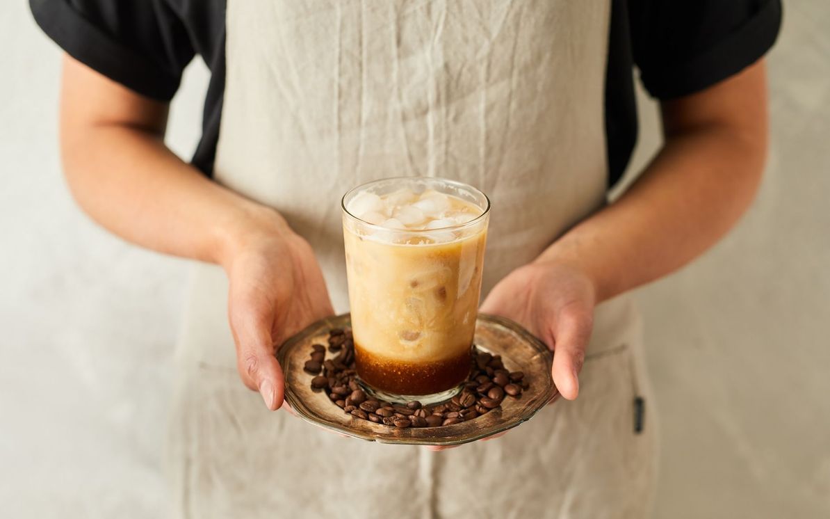 Oseba drži v rokah podstavek s kozarcem napitka Cold brew latte
