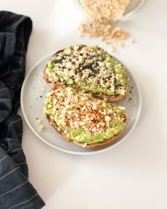 avokado kruhek z veganskim parmezan posipom, serviran na krožniku na beli podlagi s črno krpo